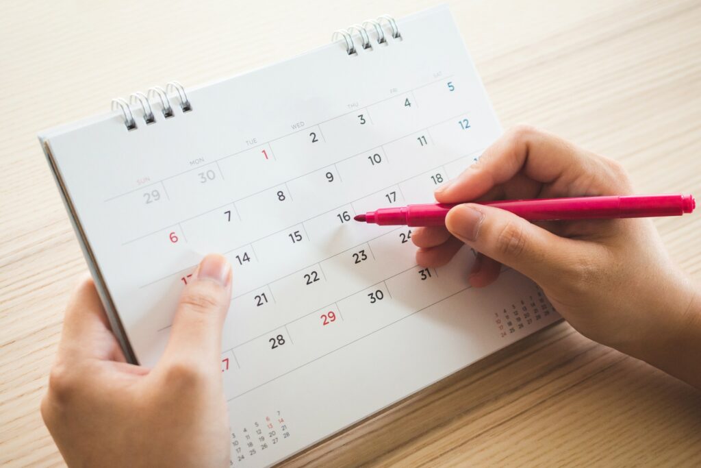 Deux mains tenant un carnet calendrier et un stylo rouge